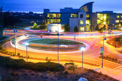 Long exposure of car lights going around a roundabout with a library in the background.