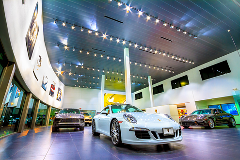 Various Porsche models adown a showroom floor in a big wide angle photo with lots of lights.