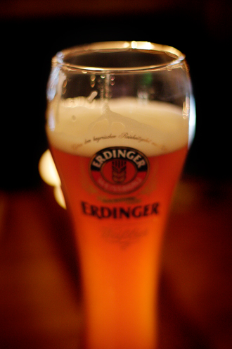 A pint of Erdinger ale glowing and backlit in a sexy glass in a dark pub. 