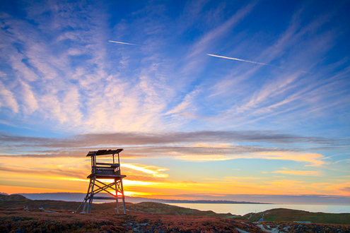 A World War II army watch tower overlooks the sand dunes and Monterey Bay at sunset with the Monterey Peninsula in the background. 