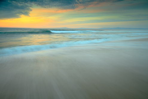 A painterly looking beach sunset in pastel colors over the Monterey Bay with Santa Cruz on the horizon. 