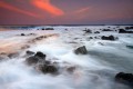 White water waves rushing through lava rock tide pools with an orange and purple dusk sky.
