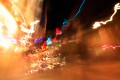 Impressionist figures rushing down the sidewalk of a busy urban street scene at night with threads and squiggles of colored light.