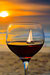 Sailboat photographed behind a glass of red wine at the beach.