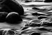 Black and white image of wet rocks in sand.