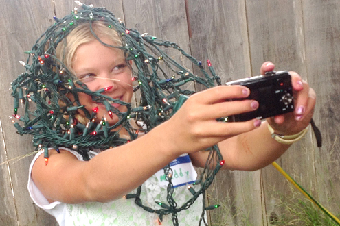 Young girl wrapped in Christmas lights and taking a self-portrait.