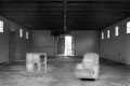 An empty warehouse with an armchair and 2 windows arranged on the floor with light coming in from side windows a door in the back.