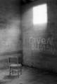 Chair facing the corner of concrete walls with light coming in from a window above and graffiti on he wall below it.