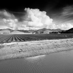 Storm clouds, mountains, tilled field, and reservoir.