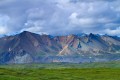 Green tundra leading to colorful mountains and dramatic clouds.