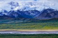Green tundra leading to dark colored mountains and dramatic clouds with stream in the foreground.