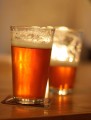 2 backlit pints of amber ale on a wooden bar.