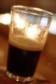Half-full pint of stout with out of focus lights in the background.