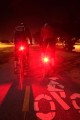 2 Bicyclists with bright red taillights light up a bike lane at night.