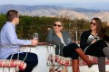 3 people sip wine on a patio with mountains in the background.