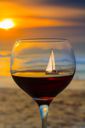 A still life composition at Marina State Beach of a glass of Pinot Noir from a nearby winery at sunset with a Monterey Bay sailboat digitally added inside the glass. Concept by Richard Hughett, W&T Publisher. 