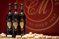 3 wine bottles on a bar surrounded by wine corks in front of a red wall with CM logo.