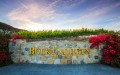 Boekenoogen sign with gold metal letters on a fieldstone wall with vineyards above and red flowers on the sides at sunset.