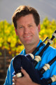 Man in blue shirt with bagpipes in a vineyard.