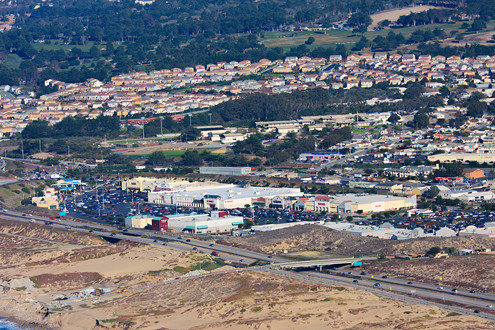 Aerial view of Sand City’s beach and shopping center, Seaside High School, Bayonet Black Horse Gold Courses, and Seaside Highlands housing on the former Fort Ord with Highway 1, Tioga Avenue overpass and Playa Avenue underpass beach accesses. 