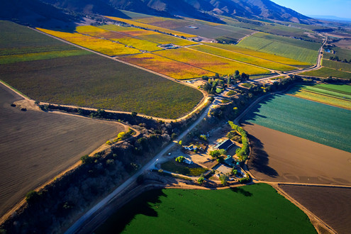 Flying between 200-1,500 feet above the famous Santa Lucia Highlands AVA in Monterey County’s Salinas Valley, this aerial photo includes Pinot Noir and Chardonnay vineyards of Pessagno 4 Boys, Morgan Double L, Lucia Highlands/Fogstone, Estancia Stonewall, Talbott Sleepy Hollow, and Kelly’s with Pessagno Winery in the foreground along the River Road Wine Trail, and Santa Cruz and the Monterey bay in the distant background. 