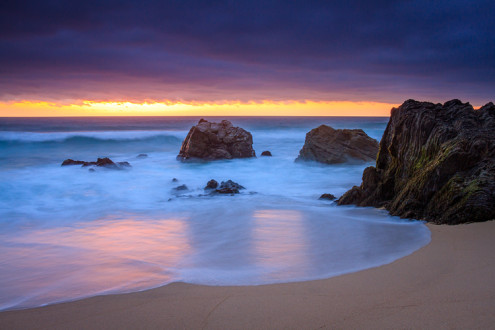 The sun sets behind a low cloud bank leaving a sliver of golden light washed across the wet rocks and sand at this Big Sur beach. Z Photo Game Card™ No. 129 