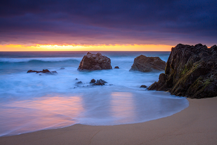 Dusk light glows off the ocean and rocks and wet sand.