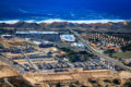 Aerial photo of half-completed development project including a theater, big box shopping center, commercial offices, medical facilities, single and multi family housing, hotel, and restaurants with the Fort Ord Dunes State Park and Monterey Bay in the background.