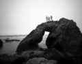 Ghostly figures standing atop a rock arch with misty ocean around them.