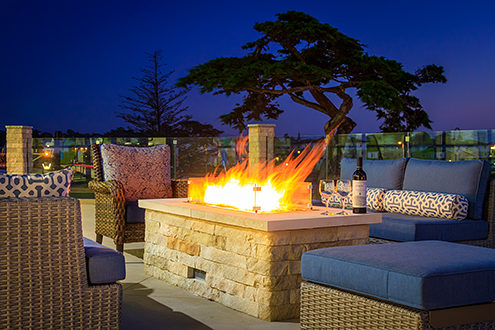 Fire tables and seating line the patio with a sunset view over Fort Dunes State Park and Monterey Bay. 