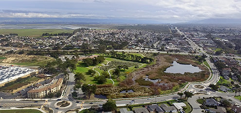 Looking east over the Reservation Road roundabouts, Locke-Padden Park and Pond, Marina Library, Del Monte Boulevard, and the city’s northeastern neighborhood. FAA certified sUAS/Drone photography.  