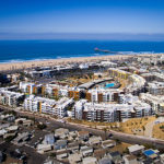 Drone photo of a city-block-size apartment complex near the beach and a pier.