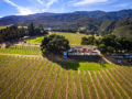 Aerial photo from about 100 feet above a vineyard looking at the tasting room festivities with vineyards and mountains in the background.