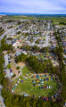 Aerial photo from a drone aircraft of a car show in a park near a residential neighborhood with fram fields in the background.