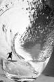 Surfer inside a wine glass riding a wave of sparkling wine as it swishes around the glass.