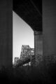 B&W photo looking through the concrete structures of a freeway to a steel bridge.