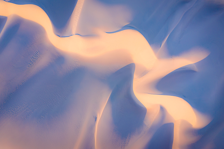 Abstract of warm sunrise light and cool shadows mix and blend across sand dunes.