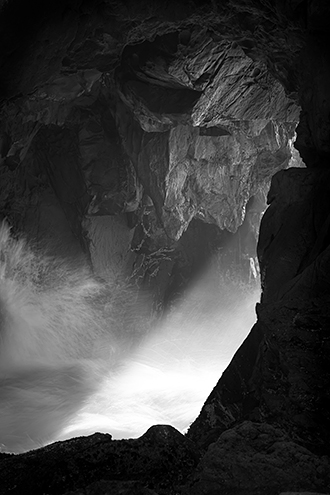 A beam of late afternoon light pushes through the ocean mist of breaking waves in a sea cave. 